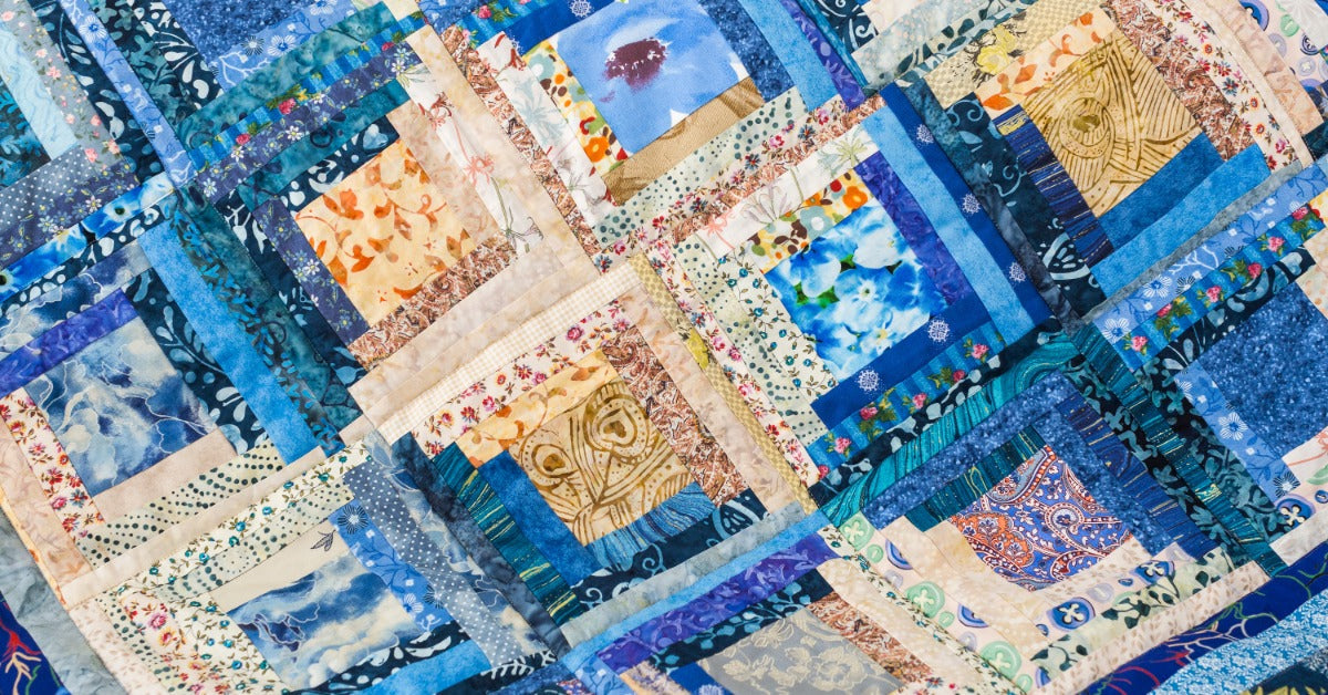 A quilt is made from square blocks with blue, cream, tan, and floral fabric strips. Each block has layered borders.