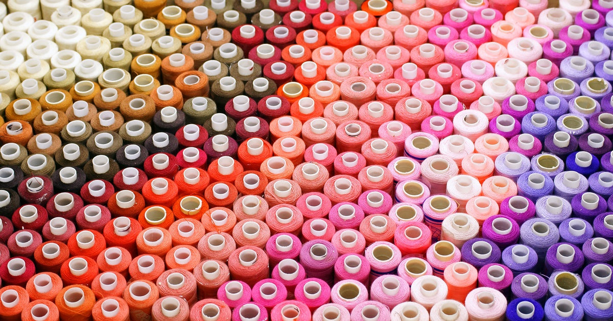 Rows of embroidery thread spools are arranged by color, moving from cream and tan shades to red, pink, and purple.