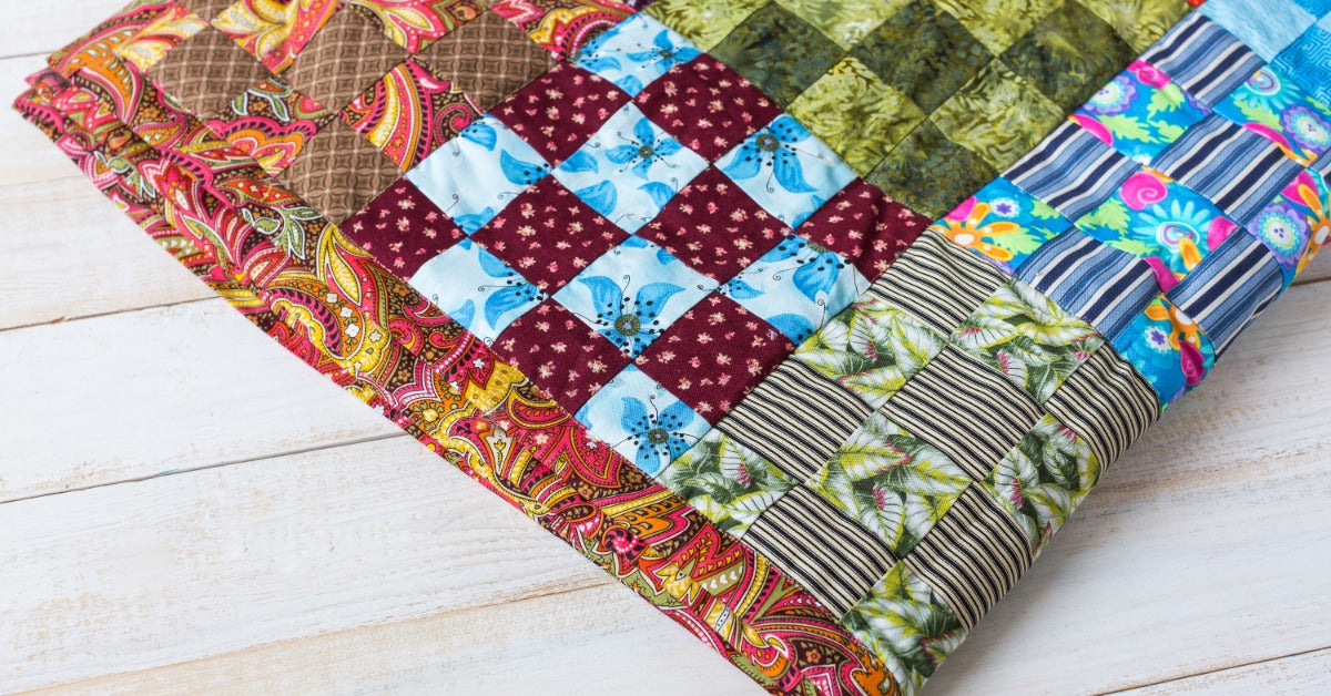 A patchwork quilt has multicolored fabric blocks. Several sections use checkerboard patterns with contrasting prints.