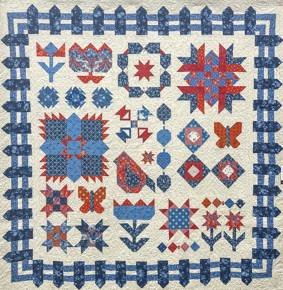 Quilt with red, and blue geometric patterns formed into flowers, a bird, butterflies and fenceposts on a light background