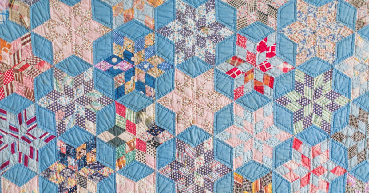 A quilt has repeating angular star patterns. The blocks combine floral prints, checks, stripes, and other patterns.