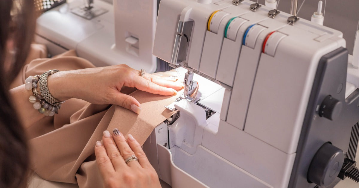 A person guides fabric through a serger while stitching the edge. They hold the material flat near the presser foot.